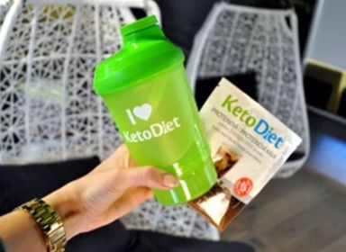 Žena drží v ruke zelený shaker KetoDiet a proteínovú ľadovú kávu s čokoládovou príchuťou.