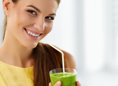 Mladá žena drží v ruce zeleninové smoothie a usmívá se.