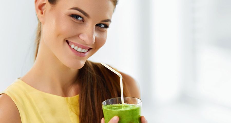 Mladá žena drží v ruke zeleninové smoothie a usmieva sa.