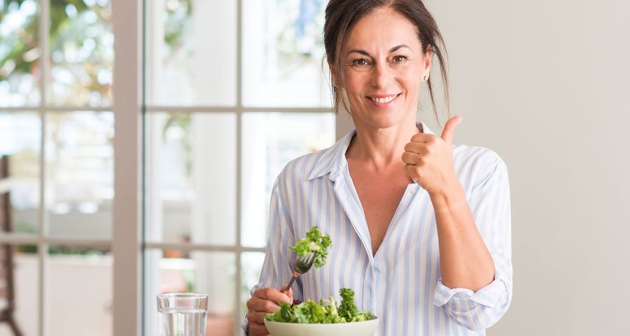 Žena v bielej košeli sedí ustolu a jej vidličkou varenou brokolicou. Existujú spôsoby, ako sa pobiť so sacharidovou chrípkou.