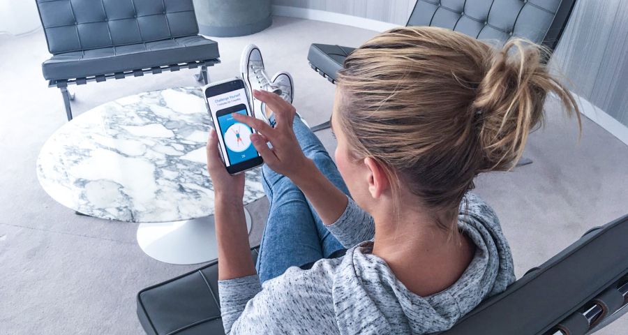 Žena sedí doma na gauči a prohlíží si aplikace na hubnutí ve svém mobilu.