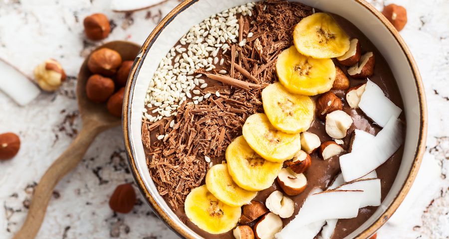 Proteínová kaša s čokoládovou príchuťou zdobená kokosom, semienkami, strúhanou čokoládou, lieskovými orechmi a kolieskami banánu.