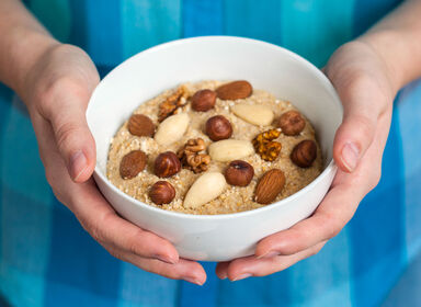 Žena drží v ruce porcelánovou misku s kaší a ořechy. Jak můžou ořechy pomoci při hubnutí?